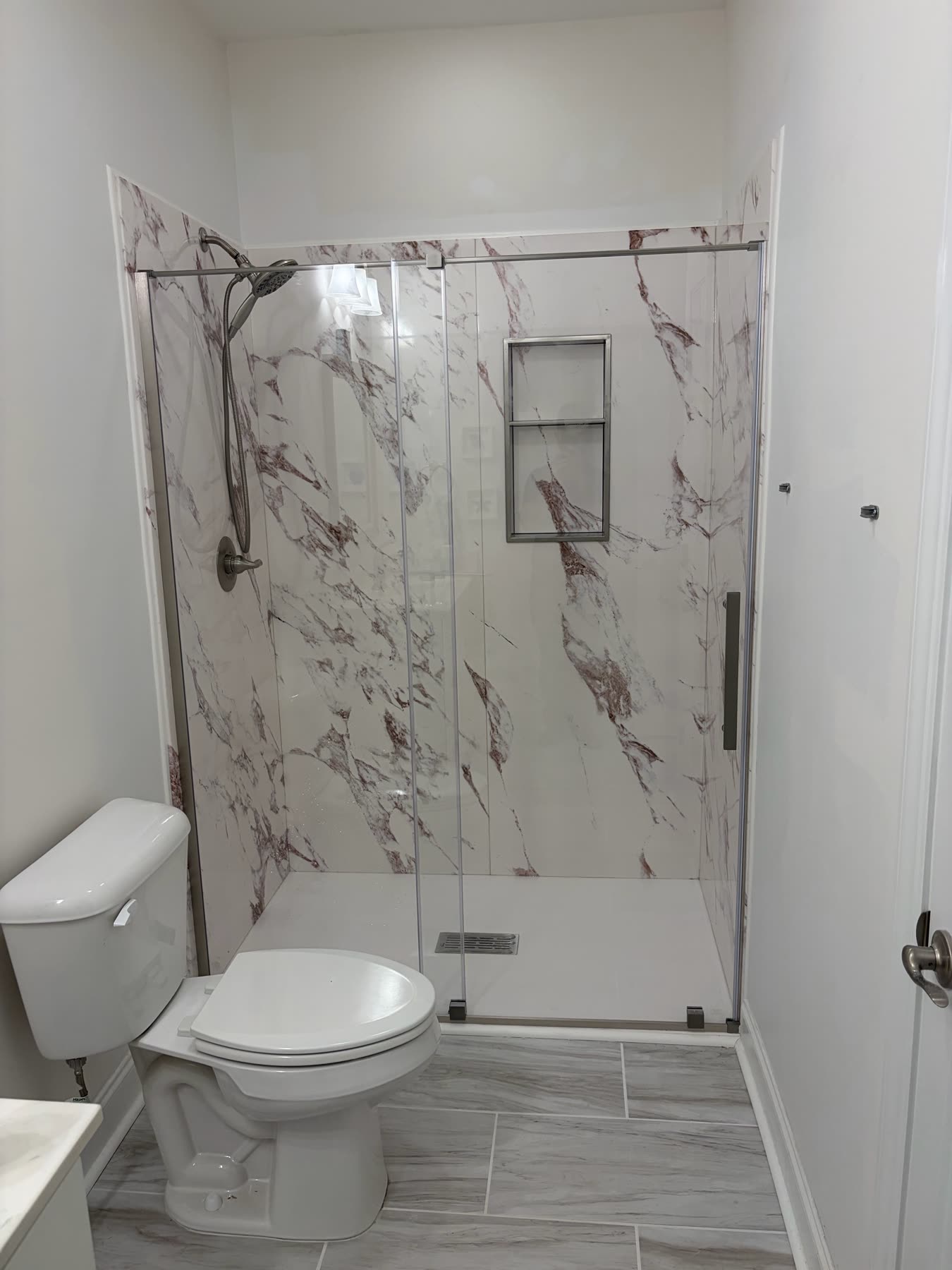 Walk-in shower with burgundy-veined marble-look panels, chrome fixtures, and a white toilet in the foreground