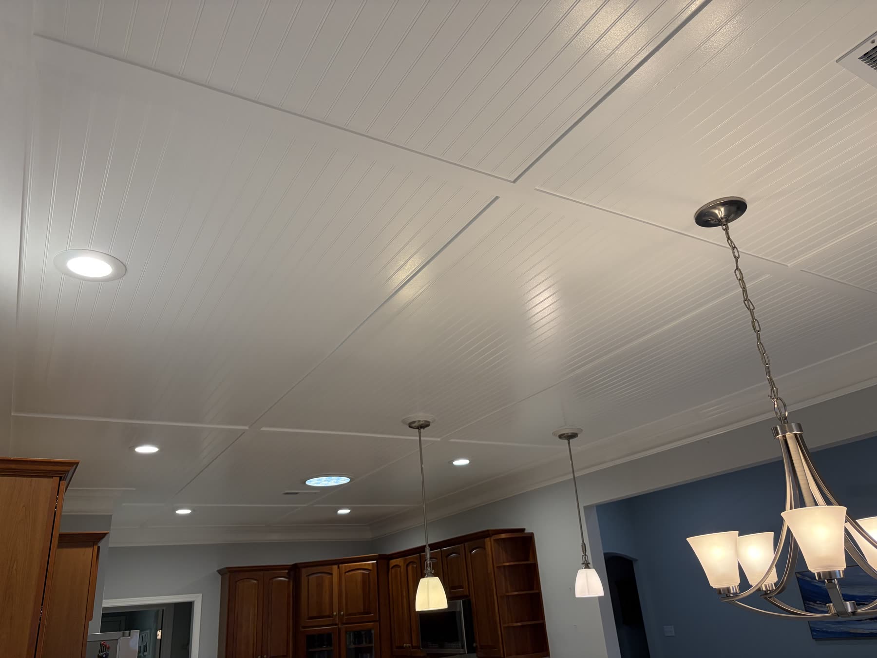 Coffered white beadboard ceiling with pendant lights, a skylight, and dark wood kitchen cabinets