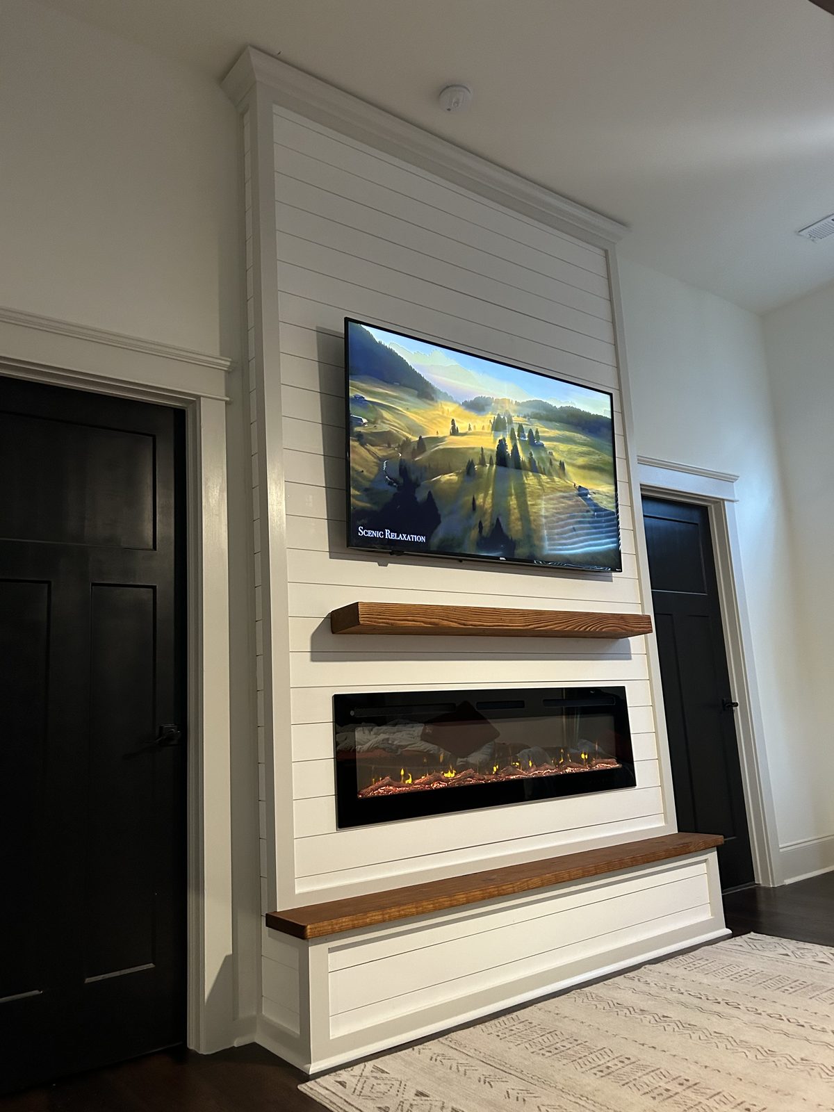 White shiplap fireplace and TV wall with a wood mantel, electric insert, and matching bench between dark interior doors