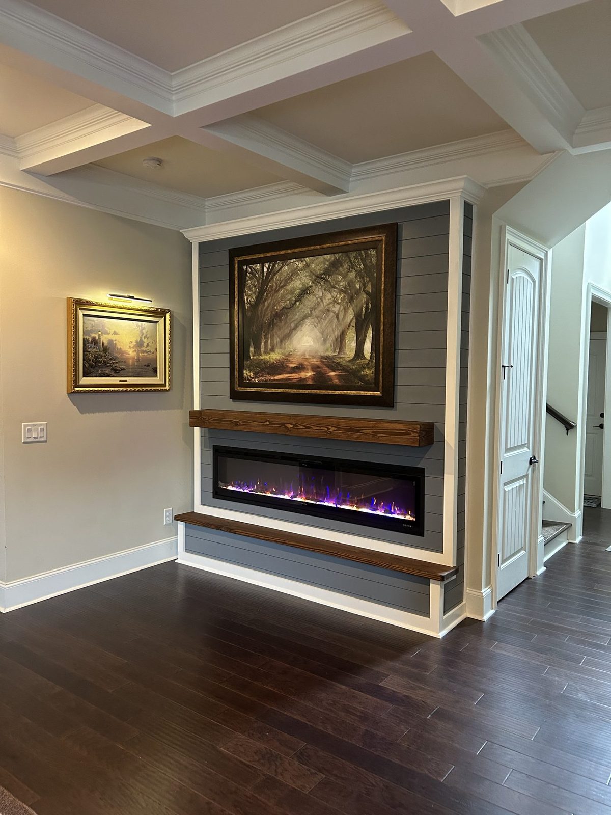 Fireplace built-in with blue-gray shiplap, dark wood mantel and hearth, coffered ceiling, and art above