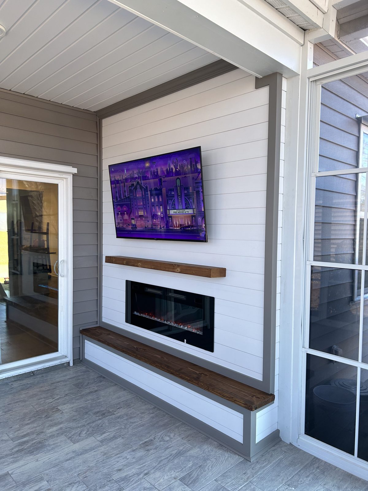 White shiplap fireplace and TV wall in a sunroom or porch with grey siding and light tile