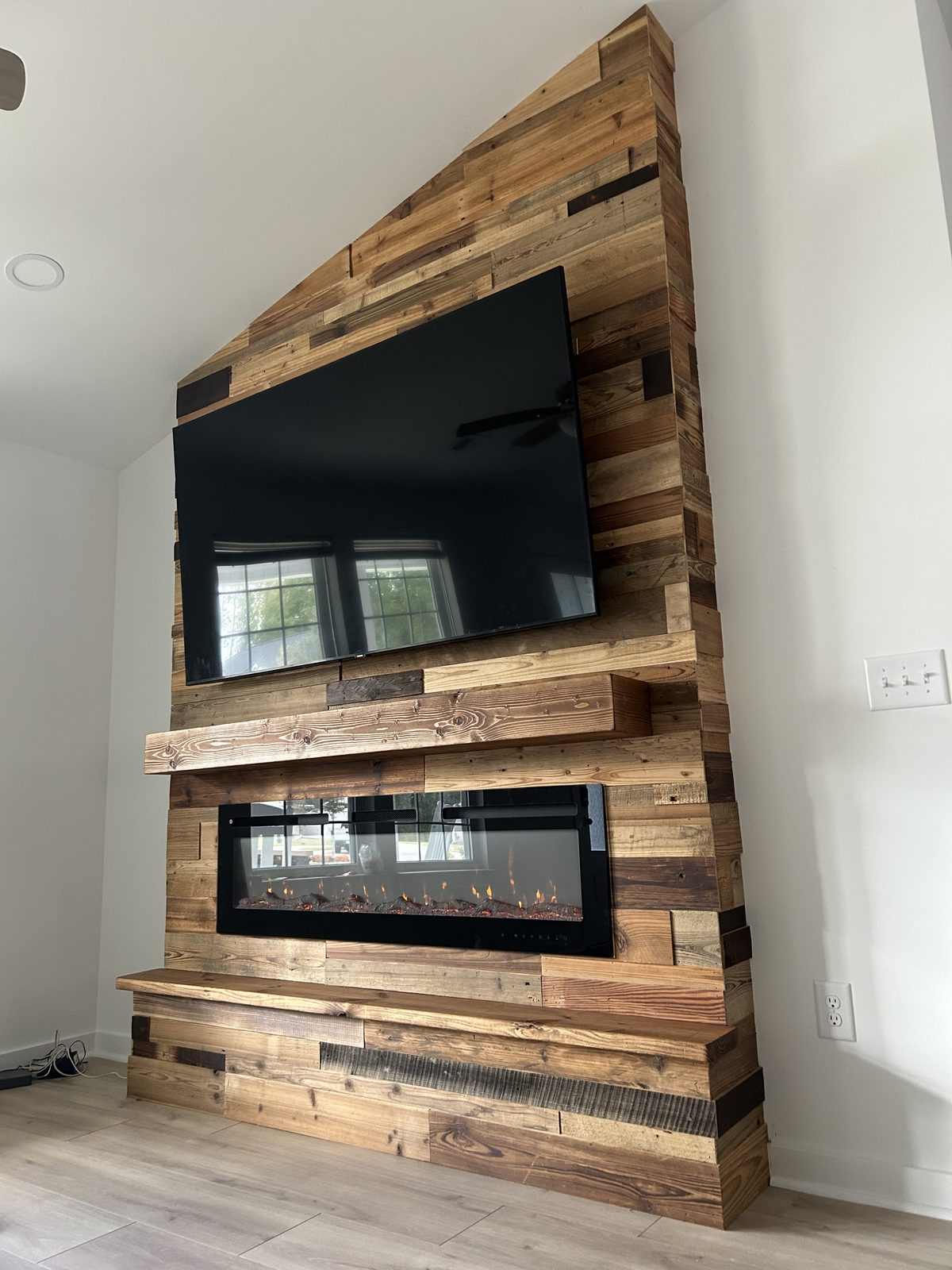 Vaulted reclaimed wood plank fireplace and TV wall with a rustic mantel and linear insert
