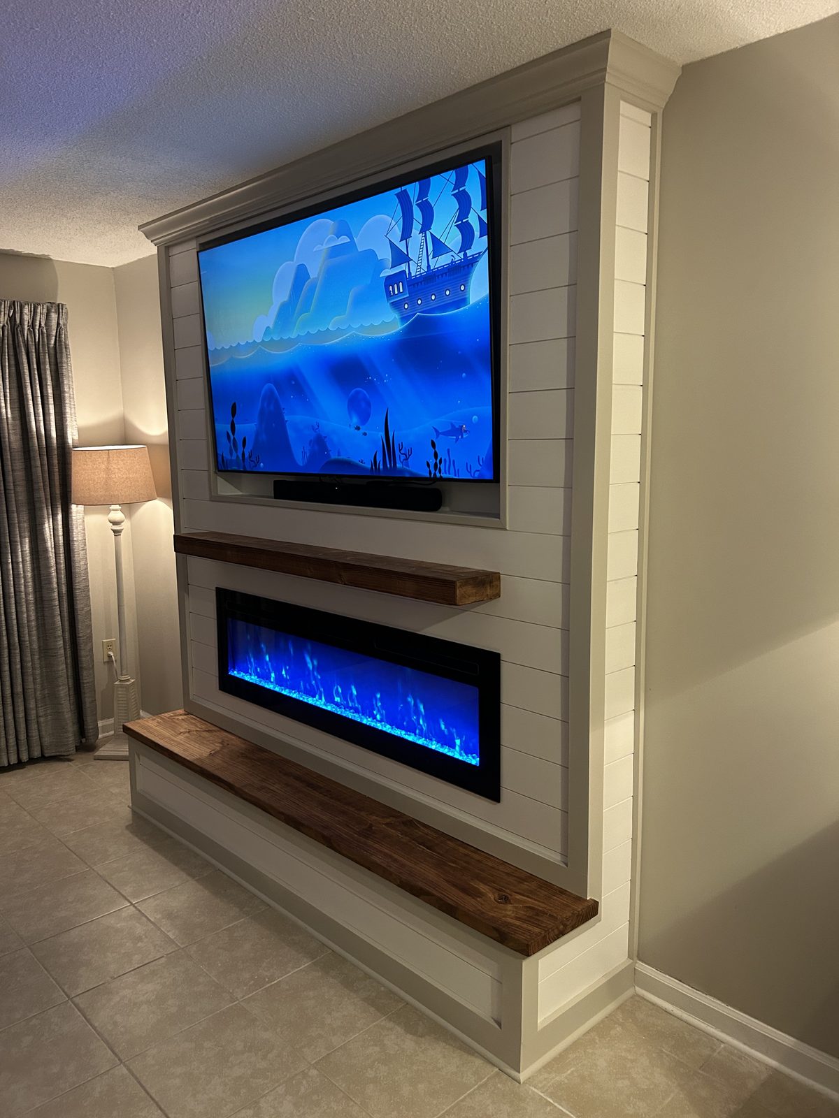 White shiplap fireplace and TV wall with a rustic mantel, soundbar, electric insert, and tile floor