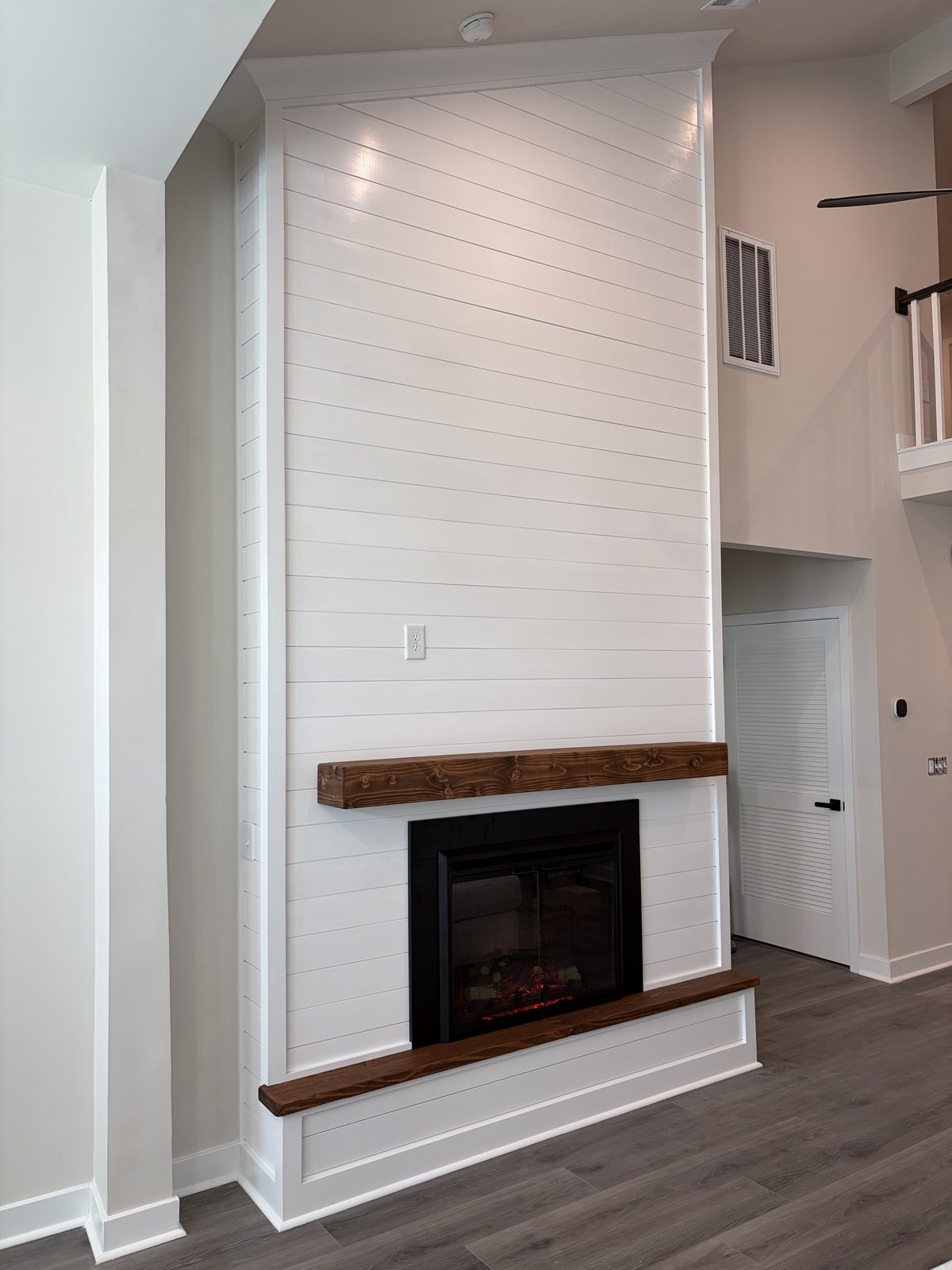 Vaulted white shiplap fireplace wall with a rustic wood mantel and hearth, ready for a TV