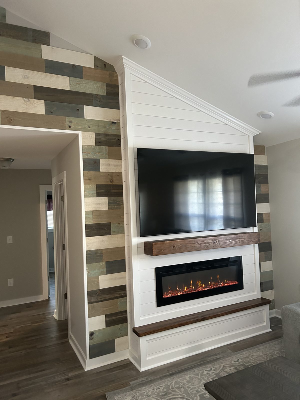 Vaulted white shiplap fireplace and TV wall beside a multi-tone reclaimed wood plank wall