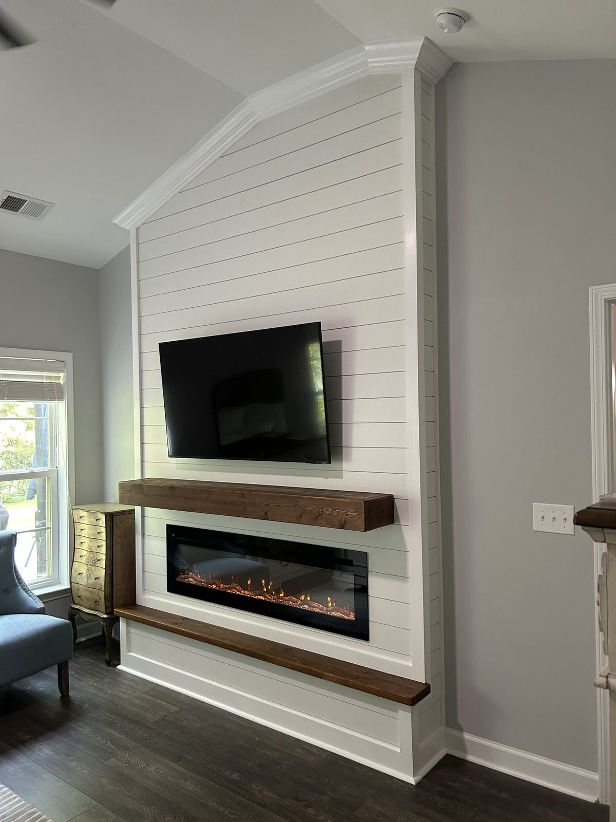 Floor-to-ceiling white shiplap fireplace and TV wall cut to a vaulted ceiling, with a rustic mantel, electric insert, and dark hearth