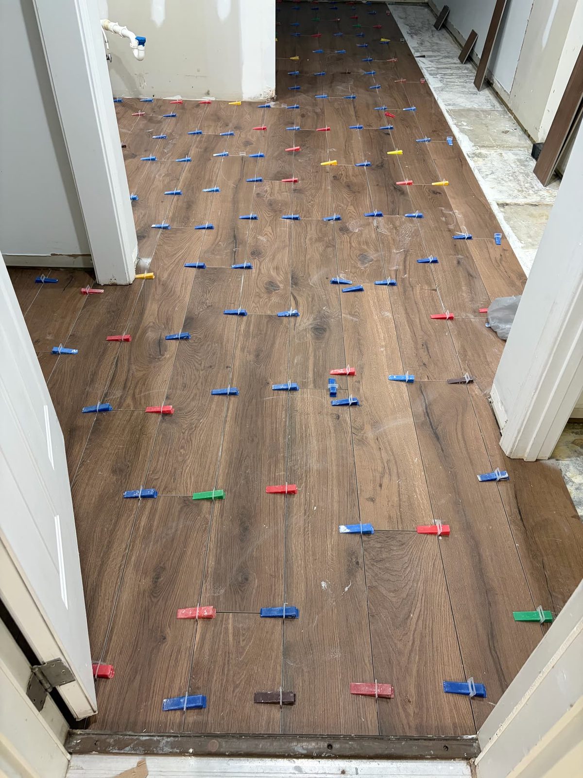 Wood-look plank floor being laid with tile leveling clips and colored wedges in a hallway