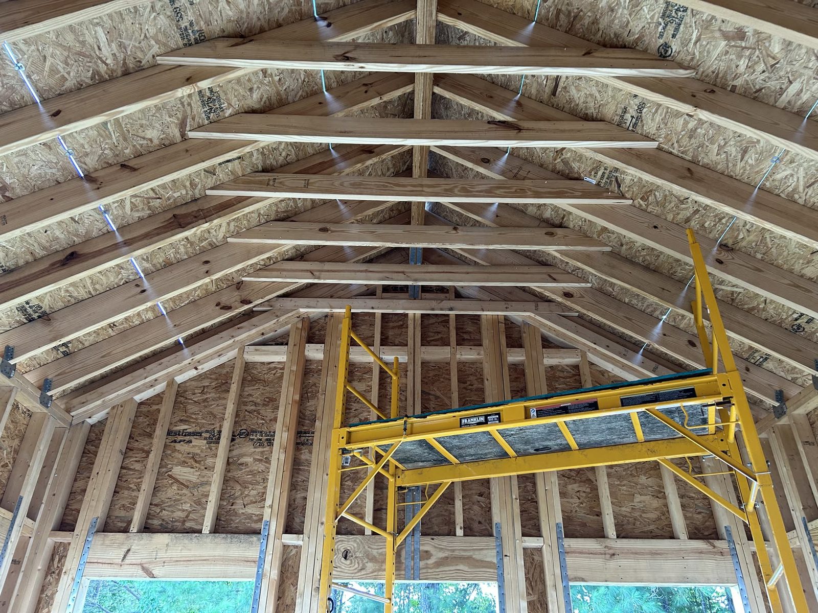Interior addition framing with rafters, ridge beam, wall studs, and a yellow scaffold