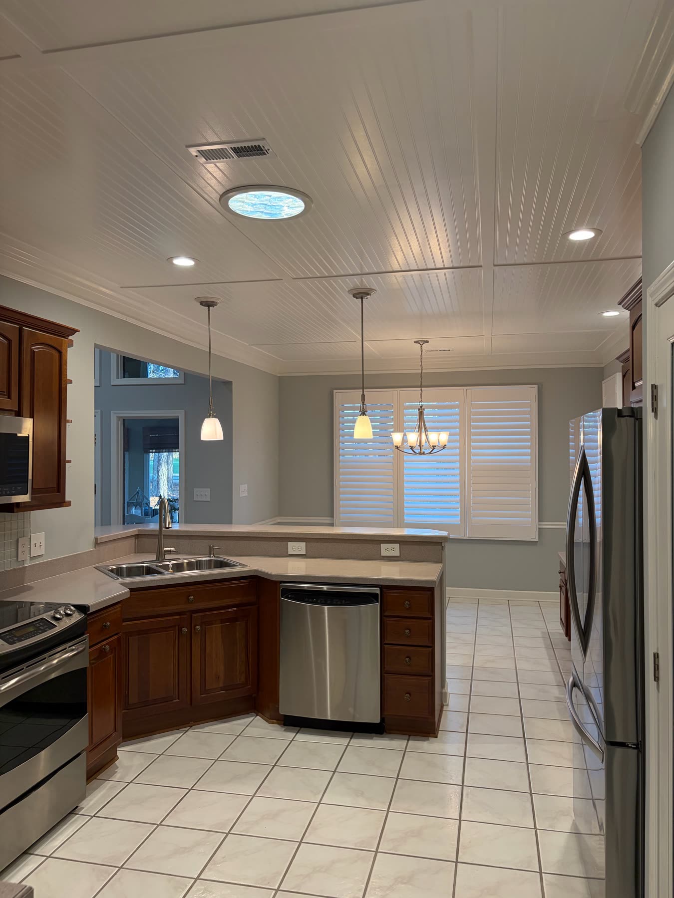 Kitchen with dark wood cabinets, beadboard ceiling, stainless appliances, and a pass-through to the living room