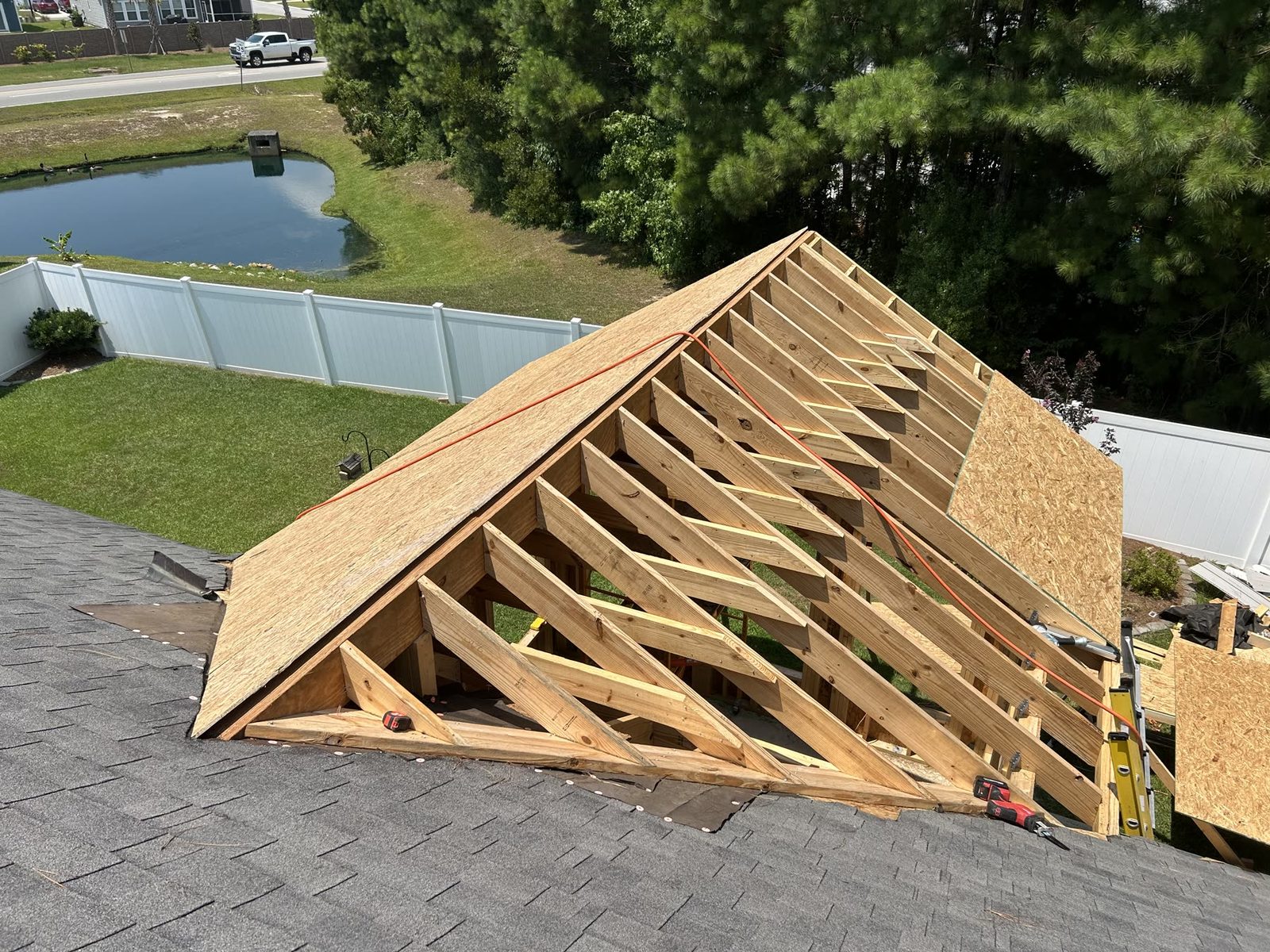 Roof framing in progress with rafters and OSB sheathing over existing shingles