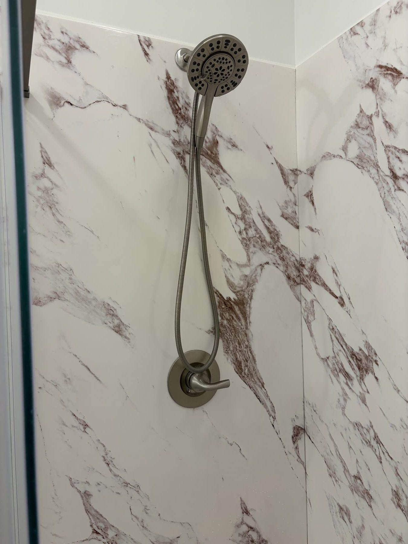 Close-up of a shower valve and handheld spray on burgundy-veined marble-look wall panels