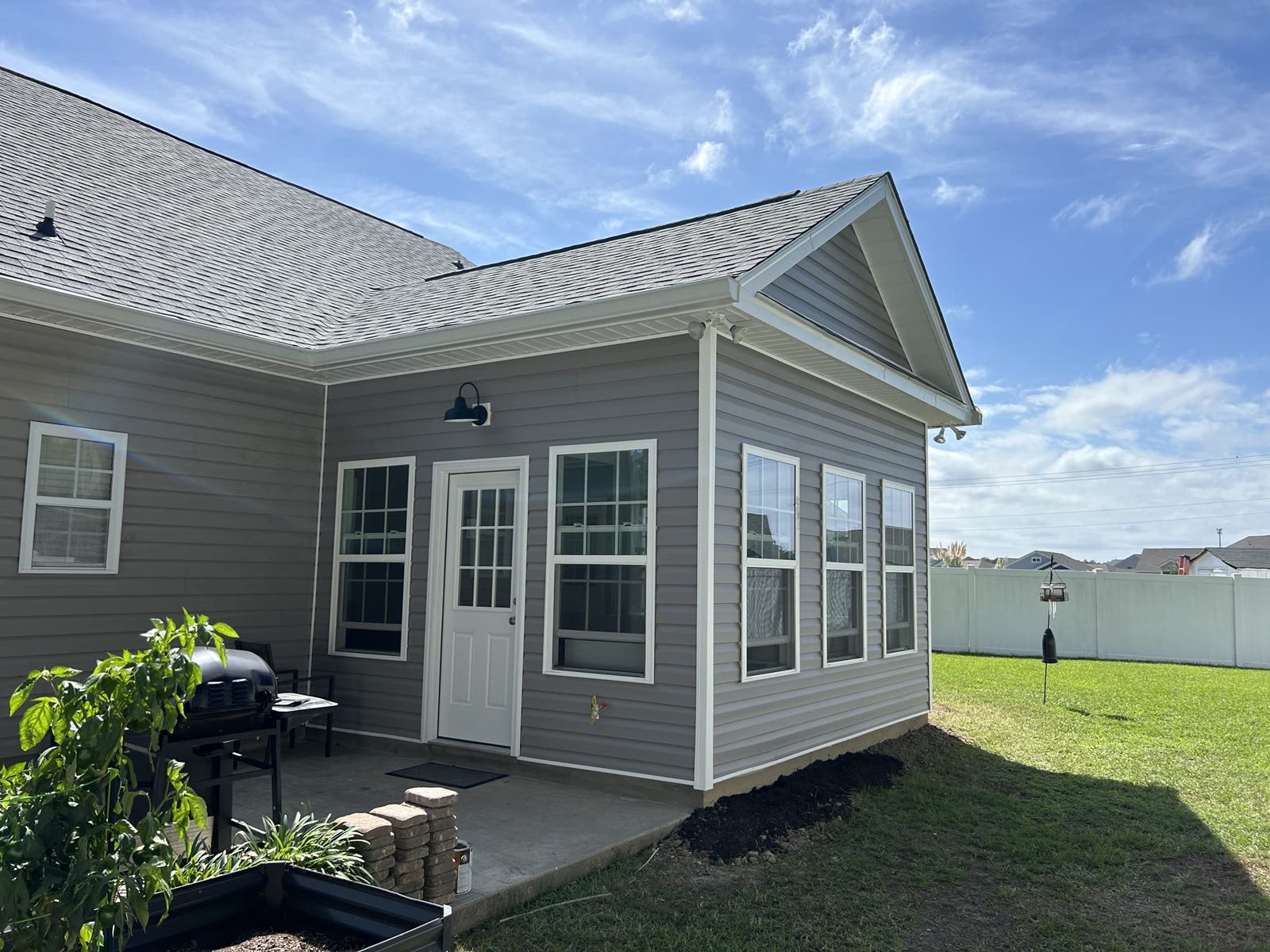 Sunroom addition from the outside with grey siding, white trim, gable roof, and patio