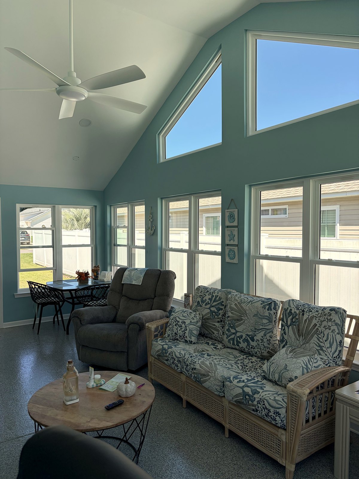 Furnished gable sunroom with tall teal walls, angled gable windows, a recliner, and a wicker sofa