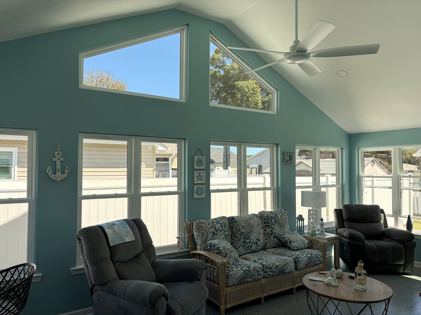 Furnished gable sunroom addition with teal walls, trapezoid gable windows, a vaulted ceiling, a ceiling fan, and a wicker sofa