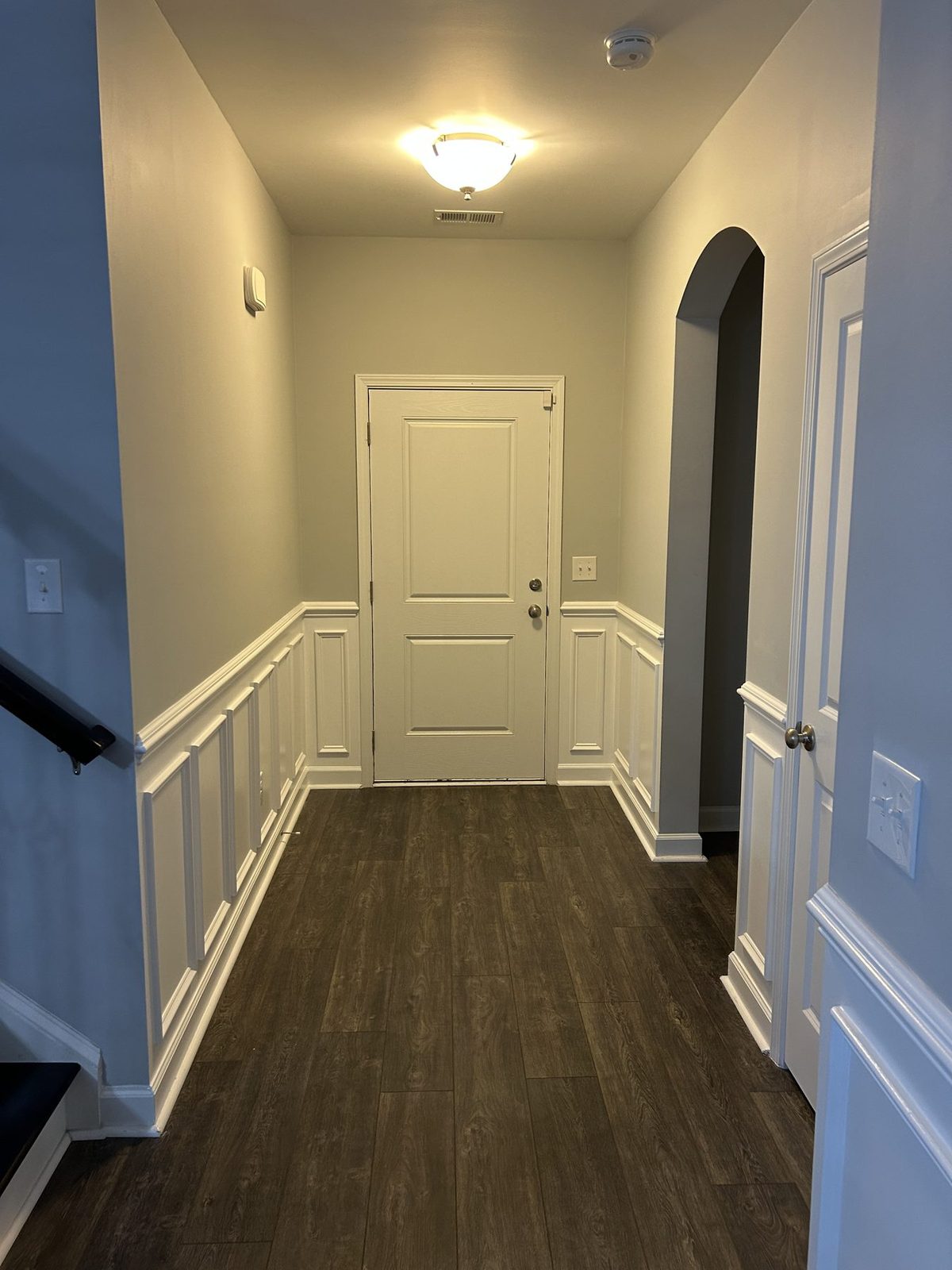 Entry hallway with white picture-frame wainscoting, front door, and an arched opening