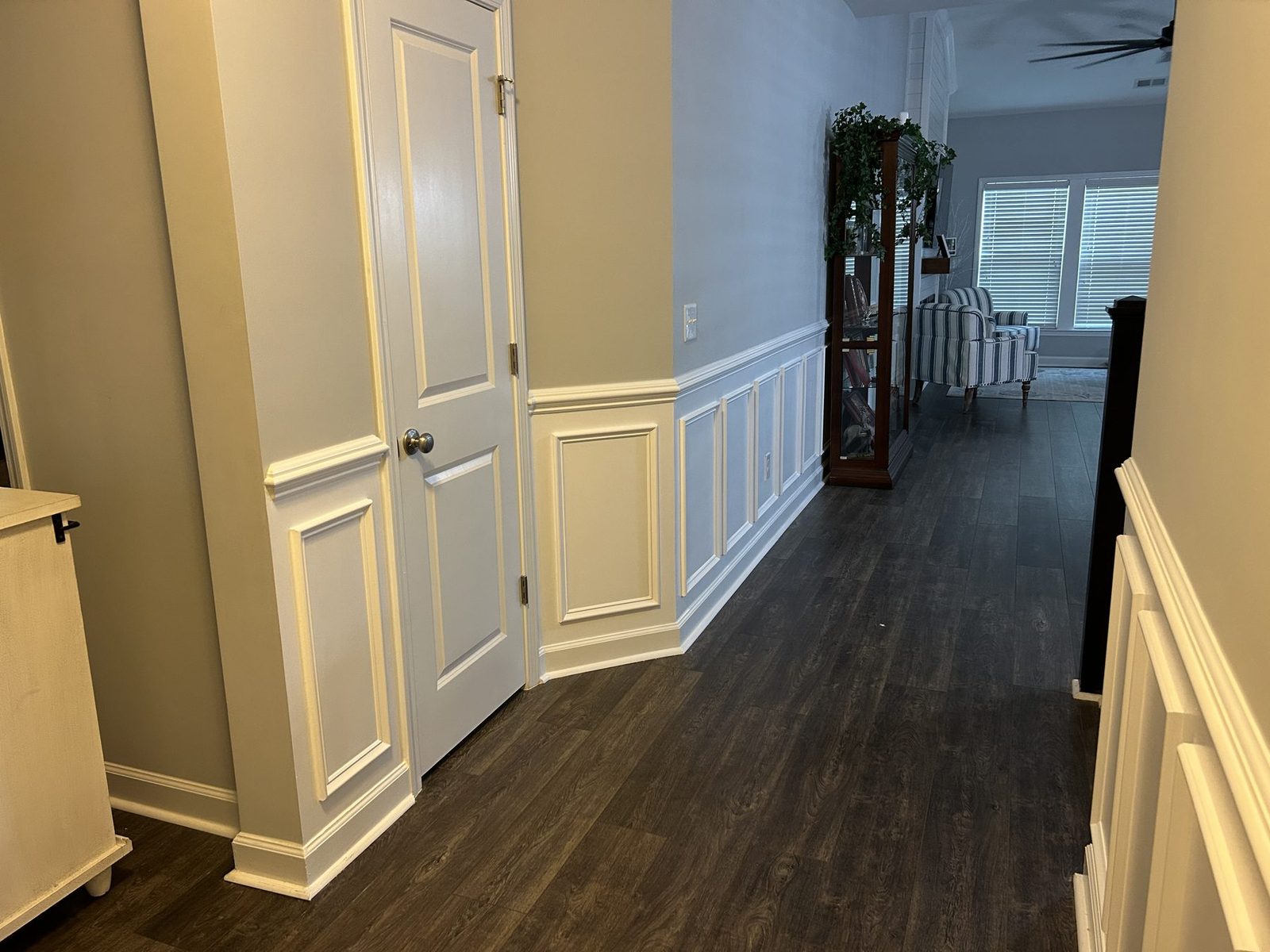 Hallway with white picture-frame wainscoting looking into a living room