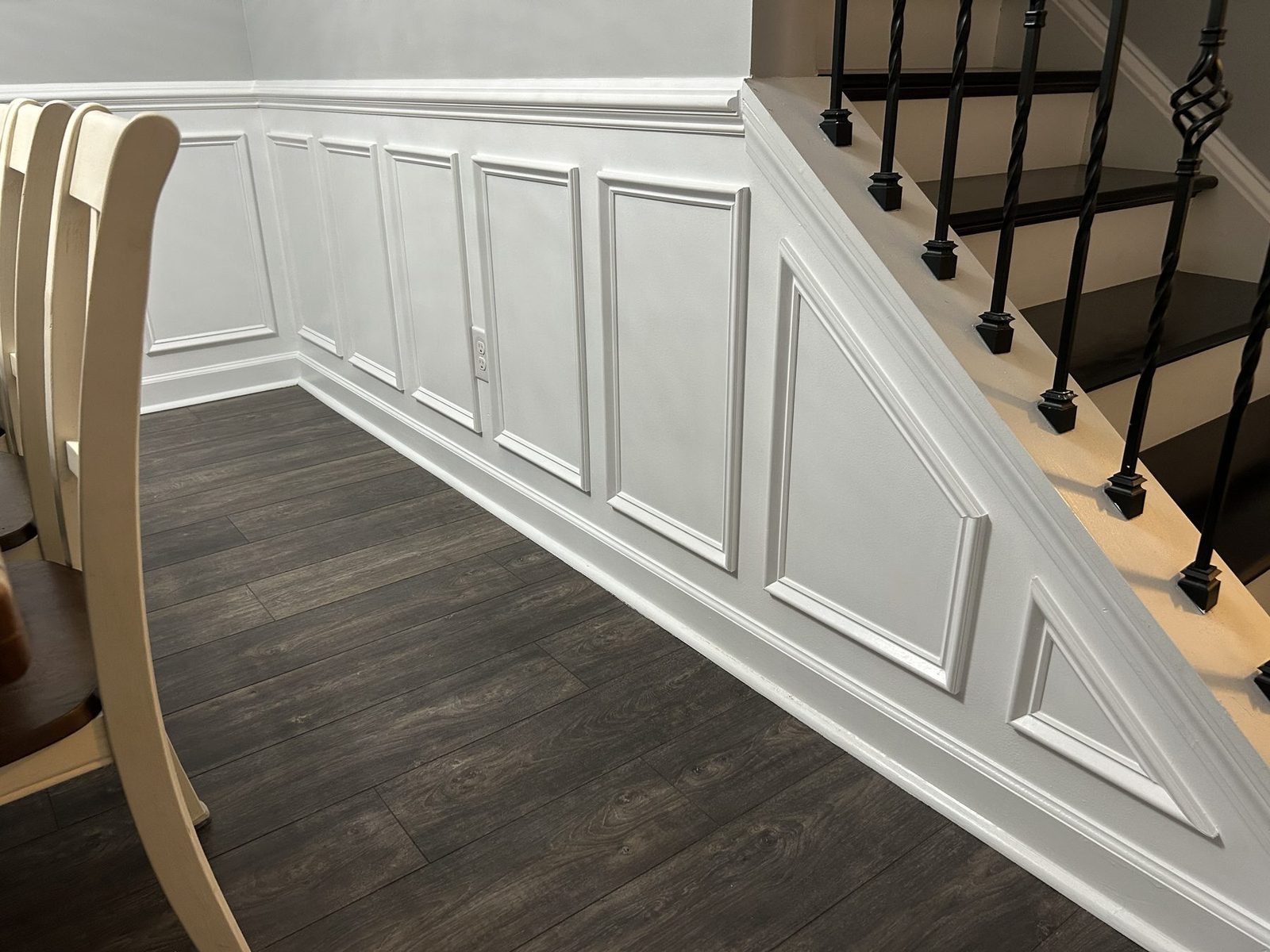 White picture-frame wainscoting custom-cut under a staircase with black iron spindles